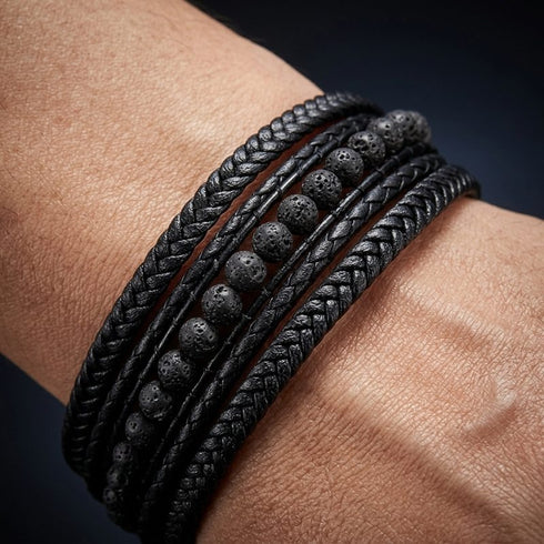 Detailaufnahme eines schwarzen Herren Lederarmbands mit Lavastein Naturstein Perlen und geflochtenem Leder am Handgelenk