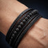 Detailaufnahme eines schwarzen Herren Lederarmbands mit Lavastein Naturstein Perlen und geflochtenem Leder am Handgelenk