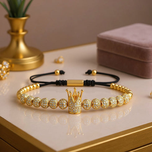 Goldenes UNIQAL Crown King Armband mit funkelnden Zirkonia-Steinen – edles Accessoire auf einem modernen Tisch-Setting, perfekt als Geschenk.