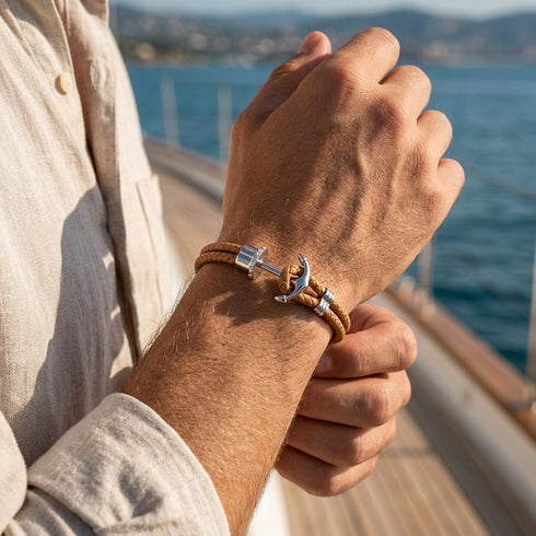 Maritimes Herrenarmband mit silberfarbenem Edelstahl Anker und braunem Leder vor einer maritimen Kulisse