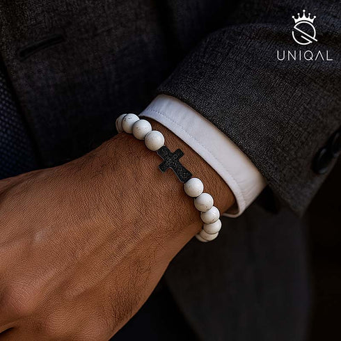 Edelsteinarmband mit weißen Howlith-Steinen und schwarzem Kreuzanhänger.