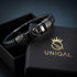 ACE OF SPADES BLACK Lederarmband mit geflochtenem schwarzem Leder und Totenkopf im Pik-Symbol, in einer UNIQAL Geschenkbox präsentiert