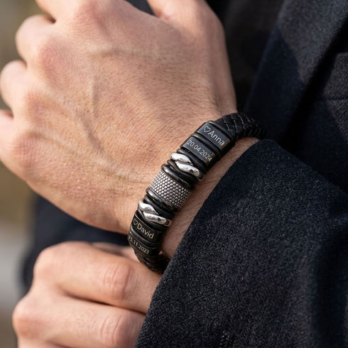 UNIQAL BLACK MAMBA Lederarmband mit gravierten Namen, Daten und Herzen am Handgelenk zu einem dunklen Sakko.