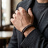 Mann mit grauem Sakko und dunklem Pullover trägt das braune BROWN BRAID Lederarmband am Handgelenk