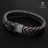 BROWN BRAID Lederarmband in liegender ovaler Ansicht mit dunklem Edelstahlverschluss und UNIQAL-Logo auf schwarzer Oberfläche