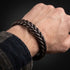 BROWN BRAID Lederarmband am Handgelenk neben einem dunkel karierten Ärmel, mit Blick auf die braune Flechtung