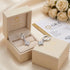 ÉCLAT von UNIQAL als Geschenkarrangement mit cremefarbener Schmuckbox, einem Ohrring im Etui und einem auf dem Deckel, neben weißen Rosen und GRA-Dokument.