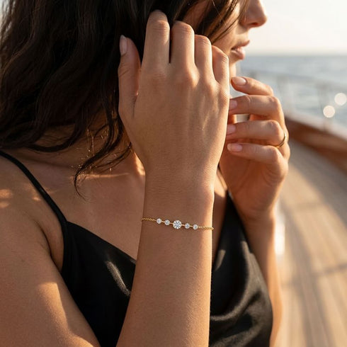 Frau mit schwarzem Top trägt das ELARA 14K GOLD Armband von UNIQAL am Handgelenk, mit fünf hell funkelnden Steinen im warmen Licht am Meer.