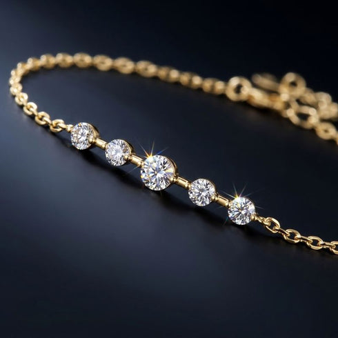 Nahaufnahme des ELARA 14K GOLD Armbands von UNIQAL: größerer Moissanit zwischen vier kleineren Steinen, mit Verlängerungskette im Hintergrund.