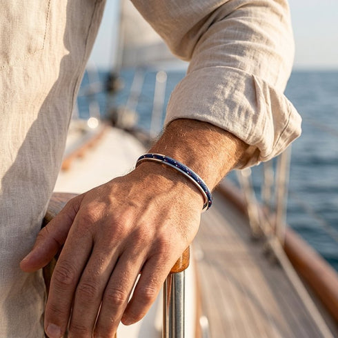 MONACO Armreif von UNIQAL mit blauem Segeltau am Handgelenk zu einem hellen Hemd, an der Reling eines Boots.