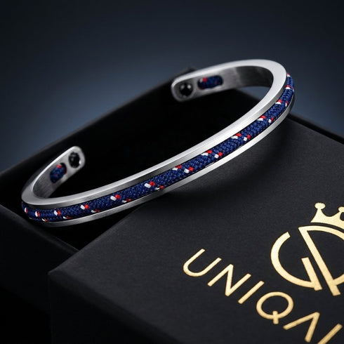 Offener MONACO Armreif mit blauem Segeltau in einer schwarzen Geschenkbox neben dem Deckel mit goldenem UNIQAL Logo.