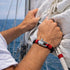 Nautische Armkette SERENITY in Rot Schwarz getragen an Bord eines Segelboots auf offenem Wasser von Uniqal Gravierbar mit Personalisiereng