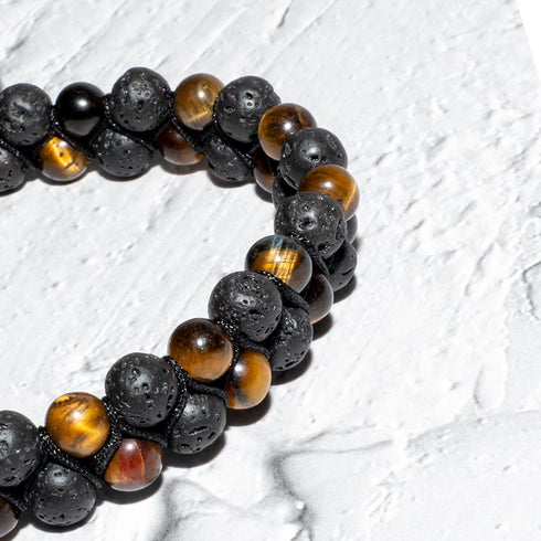 Makroaufnahme des Tigerauge-Lavastein-Armbands auf spiegelndem Untergrund – Fokus auf Energie und Struktur