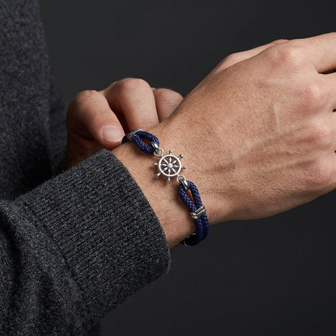 UNIQAL RHODOS Tauarmband in Dunkelblau mit silberfarbenem Steuerrad am Handgelenk zu einem grauen Strickpullover.