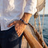 UNIQAL RHODOS Tauarmband mit Steuerrad am Handgelenk eines Mannes mit weißem Hemd an Bord eines Segelboots.