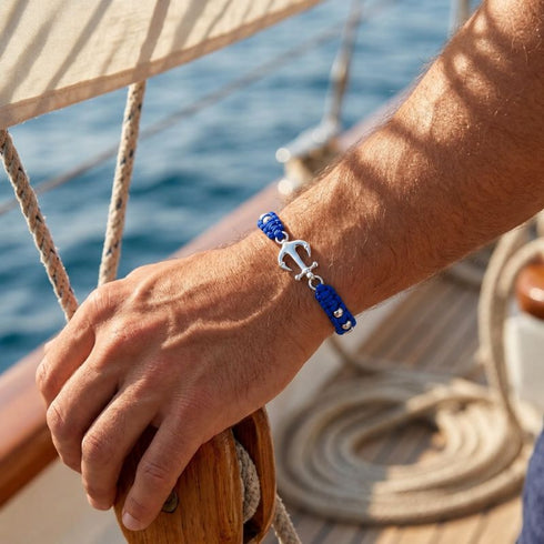 Königsblaues SARDINIA Tauarmband mit silberfarbenem Anker am Handgelenk auf einem Segelboot, mit Meer im Hintergrund – UNIQAL