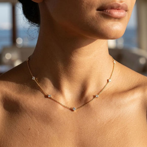 SHINE CELESTA 14K GOLD von UNIQAL aus vergoldetem 925 Sterling Silber, nah am Dekolleté fotografiert, mit klaren Steinakzenten im Sonnenlicht.