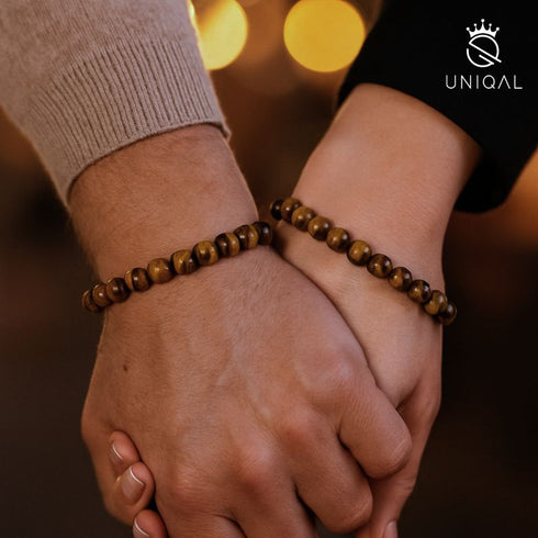 Paar hält Hände mit passenden gelben Tigerauge Armbändern im warmen Licht uniqal