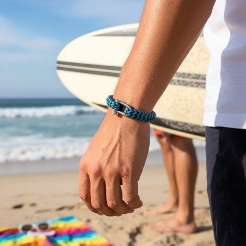 Uniqal BLUE OCEAN Armband aus blauem Segeltau in Bewegung getragen mit Meer und Strand im Hintergrund