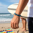 Uniqal BLUE OCEAN Armband aus blauem Segeltau in Bewegung getragen mit Meer und Strand im Hintergrund