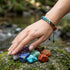 Zweireihiges Chakra Armband mit bunten Edelsteinen auf Felsen getragen mit verstellbarem Makrameeverschluss und Unisex Design