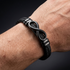 Uniqal ENDLESS BLACK Lederarmband am Handgelenk – schwarzes Herrenaccessoire mit Flechtdesign und zentralem Unendlichkeitszeichen.