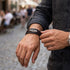 Mann mit dunklem Hemd trägt das ENDLOS Lederarmband von UNIQAL mit silberfarbenem Unendlichkeitszeichen und roten Nähten vor urbaner Kulisse.
