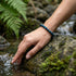 Facettiertes Falkenauge Armband auf Felsen getragen mit tiefem Farbspiel und individuell gravierbarem Makrameeverschluss