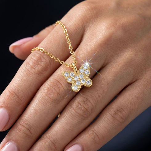 FARFALLA 14K GOLD Moissanit-Anhänger von UNIQAL auf einer Hand, mit filigraner Flügelform und feinem Steinbesatz.