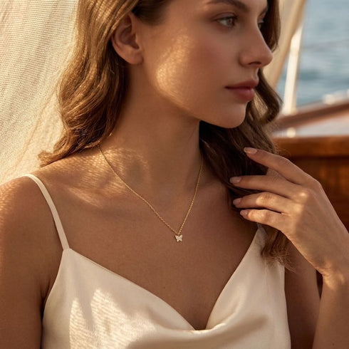 FARFALLA 14K GOLD Moissanit-Schmetterlingskette von UNIQAL am Dekolleté, mit sanftem Schimmer und leichter Silhouette.