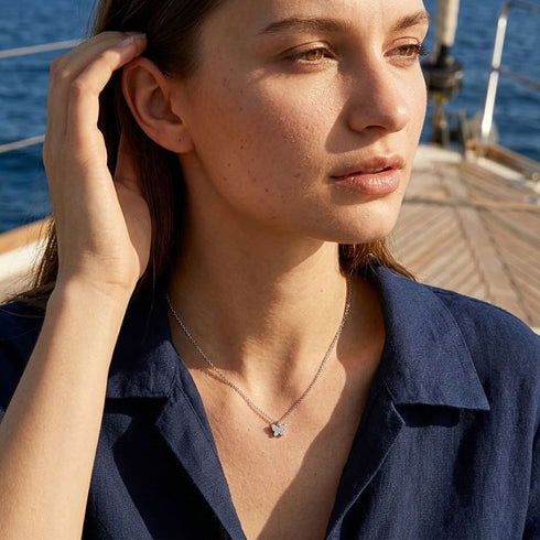 FARFALLA Schmetterlingskette mit Moissanit von UNIQAL, getragen zur dunkelblauen Bluse auf einem Segelboot im Sonnenlicht.