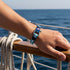 Uniqal FLUNDER nautisches Seilarmband in Türkis und Weiß am Handgelenk getragen mit Blick auf das offene Meer