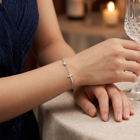 Frau mit GRACE Moissanit-Armband von UNIQAL zu dunkelblauer Abendgarderobe, die Hand an einem geschliffenen Glas bei Kerzenschein.