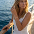 UNIQAL GRACE Moissanit-Armband an einer Frau im weißen Kleid, getragen am Geländer vor einer maritimen Kulisse im Sonnenlicht.