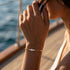 GRAZIA 14K GOLD Moissanit-Armband von UNIQAL am angehobenen Handgelenk einer Frau in heller Kleidung, aufgenommen im warmen Sonnenlicht