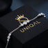 GRAZIA Moissanit-Armband von UNIQAL diagonal über einem goldenen Markenlogo, mit silberfarbenen Dreiergruppen und feinen Verbindungsgliedern