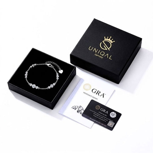 UNIQAL GRAZIA Moissanit-Armband in einer geöffneten schwarzen Geschenkbox neben dem Markendeckel, einem GRA-Bericht und einer Zertifikatskarte.