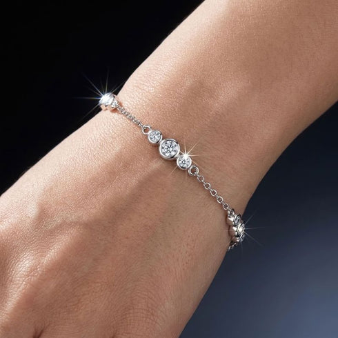Nahaufnahme des UNIQAL GRAZIA Moissanit-Armbands am Handgelenk mit runden Zargenfassungen und einem größeren Mittelstein zwischen zwei kleineren Steinen.