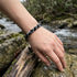 Edelsteinarmband aus Labradorit und schwarzem Turmalin am Handgelenk am Fluss getragen mit personalisierbarem gravierbarem Verschlussdetail
