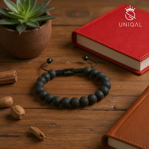 Schwarzes Uniqal Lava-Stein Armband auf Holztisch neben Notizbuch und Pflanzen, natürliches Herrenarmband im minimalistischen Stil.