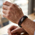 uniqal timeless Armband mit rot-schwarzen Bändern und silberfarbenem Unendlichkeitszeichen am Handgelenk beim Halten einer Tasse am Fenster.