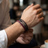 Person im weißen Hemd trägt das uniqal timeless Armband mit rot-schwarzem Flechtband und silberfarbenem Unendlichkeitszeichen in einem Café.