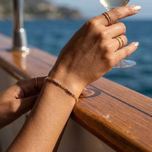 TRIA LINK 14K GOLD Moissanit-Armband von UNIQAL am angehobenen Handgelenk, kombiniert mit schmalen goldfarbenen Ringen