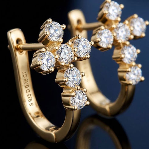 VERA 14K GOLD von UNIQAL in Nahaufnahme: vergoldete Creolen mit kreuzförmigem Steinbesatz und hellen Lichtreflexen vor dunklem Hintergrund.